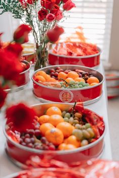 several red tins filled with different types of fruits and vegetables on a table next to flowers