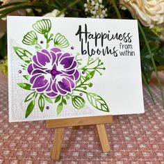 a card with flowers on it sitting on top of a easel next to some flowers