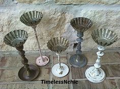 four metal candlesticks sitting next to each other on a tile floor in front of a stone wall