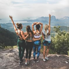 four women standing on top of a mountain with their arms in the air