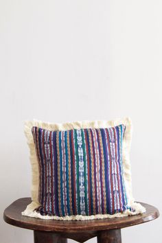 a colorful striped pillow sitting on top of a wooden table next to a white wall