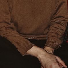 a man wearing a brown sweater and black pants sitting on a red chair with his hands in his pockets