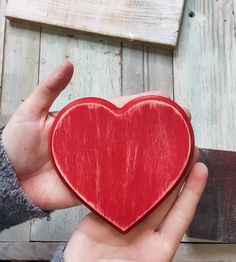 a person holding a red heart in their left hand on a wooden planked surface