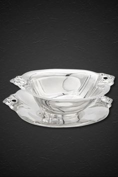 a glass bowl and saucer sitting on top of a black surface with silver accents