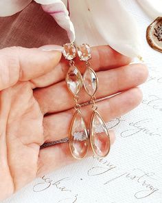 a woman's hand is holding some kind of earrings on her left hand, with flowers in the background