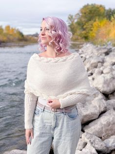 a woman with pink hair is standing by the water wearing jeans and a white sweater