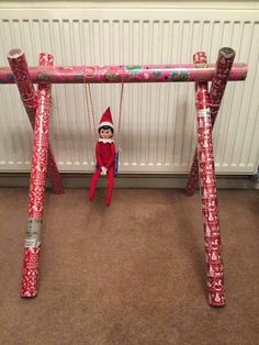 an elf is sitting on a swing made out of wrapping paper and wrapped in red tape