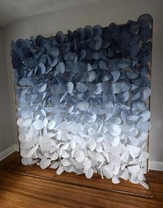 a large piece of art made out of blue and white paper flowers on a wooden floor