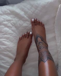 a woman's legs with tattoos on them laying on a white bedding sheet