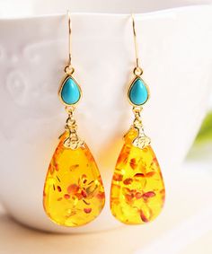 a pair of yellow and turquoise earrings sitting on top of a white cup