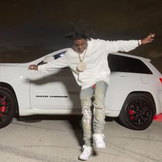 a man in white jacket and jeans standing on top of a white car with red rims