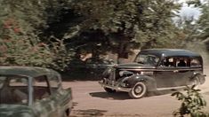 an old black car driving down a dirt road