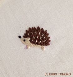 an embroidered hedge sitting on top of a white table cloth with brown trimmings