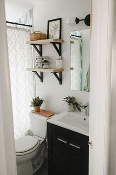 a white toilet sitting next to a bathroom sink under a mirror on top of a wooden shelf