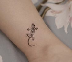 a small gecko tattoo on the left arm and foot, with a flower in the background