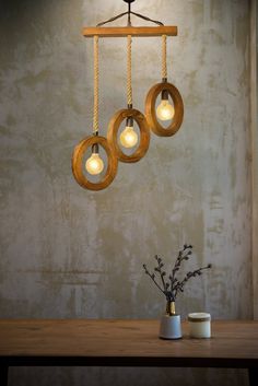 three lights hanging from a wooden beam on a wall above a vase with flowers in it