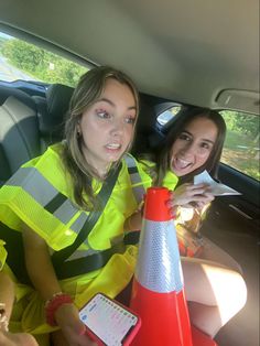 two women sitting in the back seat of a car, one holding a traffic cone