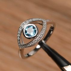 It is a London blue topaz ring. The main stone is 5mm*5mm round cut, weight about 0.6 carats.The basic metal is sterling silver and plated with rhodium.To change the metal to a solid gold (white/rose) or platinum is also available, please ask for a quotation if you want.You can also go to my shop Home for more elegant rings: https://www.etsy.com/shop/godjewelry?ref=hdr_shop_menu More London blue topaz rings: https://www.etsy.com/shop/godjewelry?ref=seller-platform-mcnav&section_id=20715039Cu 14k White Gold Topaz Birthstone Promise Ring, Anniversary White Gold Rings With Diamond Eyes, Elegant Silver Rings With Diamond Eyes, White Topaz Round Birthstone Ring, White Gold Rings With Diamond Eyes As Gift, Round Diamond Ring With Diamond Eyes As Gift, Diamond Eyes Promise Ring In Fine Jewelry Style, White Topaz Birthstone Ring, Promise White Gold Topaz Birthstone Ring