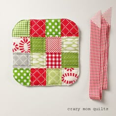 a red and green patchwork pot holder next to a piece of cloth on a white surface