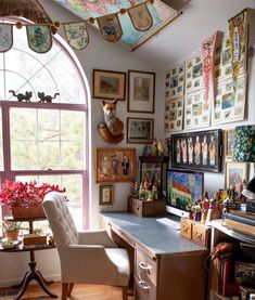 a home office with lots of pictures on the wall and desk in front of a large window