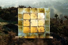 a yellow square shaped object sitting on top of a grass covered hill with trees in the background