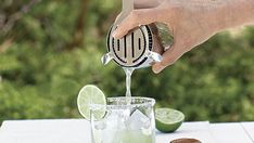 a person pouring something into a glass with limes on the table next to it