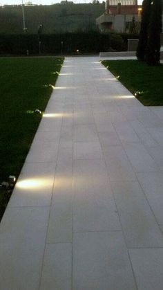 the walkway is lined with white tiles and lit up by lights in the grass area