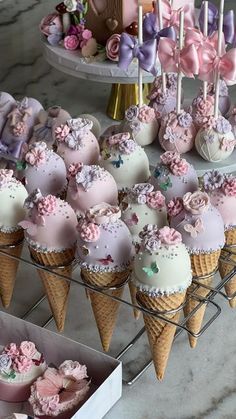 there are many cupcakes on the table and in cones with pink, purple, and white frosting