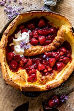 a baked dessert with strawberries and whipped cream in a pie dish on a wooden table