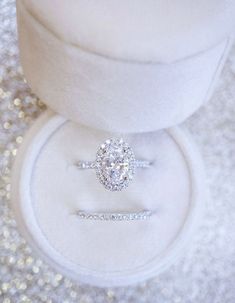 an engagement ring sitting on top of a white velvet box with glitter in the background