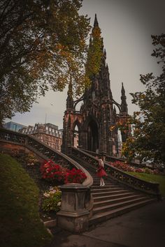 a woman in a red dress is walking up some stairs with flowers on either side