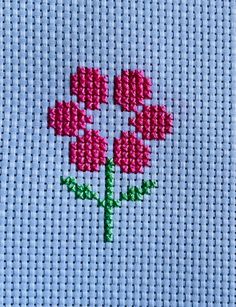 a close up of a piece of cloth with a cross stitch pattern on it and a pink flower in the middle