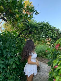 a woman is standing in front of some trees and bushes with her back to the camera