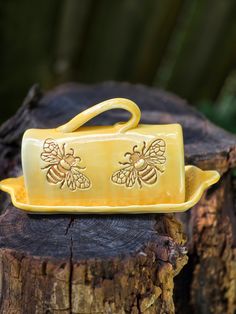 a yellow ceramic bee dish sitting on top of a tree stump next to a piece of wood