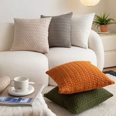 a white couch with three different colored pillows on top of it and a coffee cup next to it