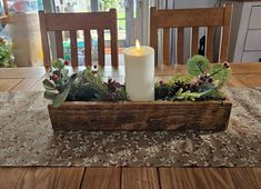 a candle is lit in a wooden box with greenery and berries on the table