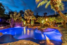 an outdoor pool surrounded by palm trees and water features a waterfall that is lit up at night