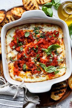 a casserole dish with tomatoes and basil on top, surrounded by other appetizers