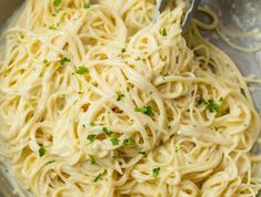 a black bowl filled with pasta and topped with parmesan cheese, chives and seasoning