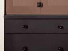 a black dresser with two drawers in front of a brown wall and wooden door on the side