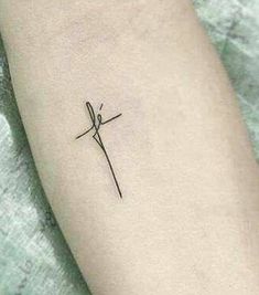 a small cross tattoo on the left inner arm, with an arrow in the middle