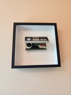 an old camera in a shadow box on the wall above it is a red flower