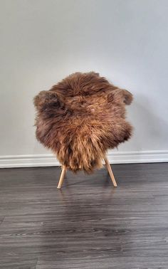 an animal skin stool on wooden legs in front of a white wall and hardwood floor