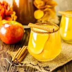 two glasses filled with apple cider on top of a wooden table next to cinnamon sticks