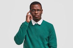 a man in a green sweater is holding his hand up to his ear and looking at the camera