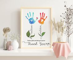 two handprints are displayed on a shelf next to vases and flowers