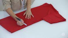 a woman is making a t - shirt out of red material with her hands and pen