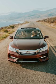 a car driving down the road with two people in it's passenger seat, and mountains in the background