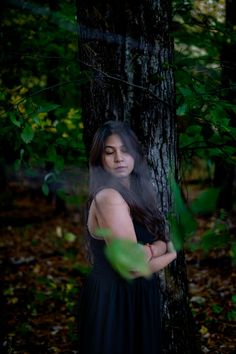 a woman standing next to a tree in the woods