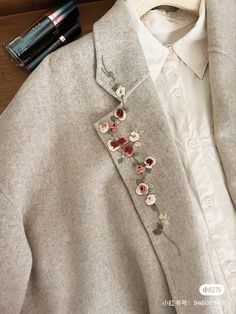 a white shirt with flowers on it next to a lipstick bottle and some other items